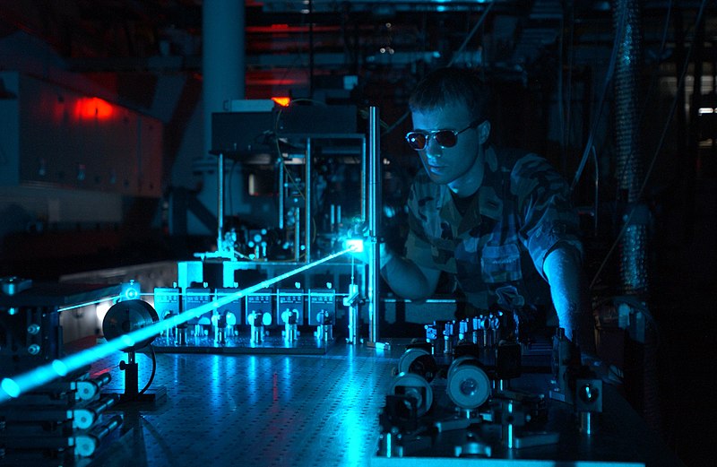 military personnel working with a laboratory laser setup utilizing a collimated laser beam